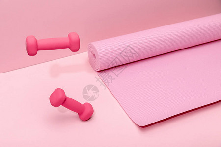 粉红色的亮哑铃悬浮在粉红色背景的橡胶健身垫图片