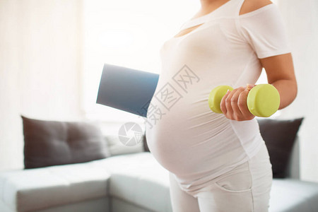 怀孕妇女在家中拿着瑜伽垫子的孕妇图片