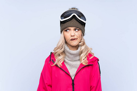 穿着滑雪眼镜的滑雪少女在孤立的蓝色背景和疑惑与混淆图片