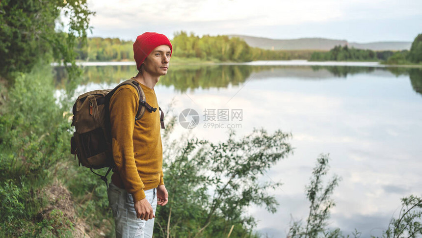 一位背着包和一顶红帽子的游客站在河边图片