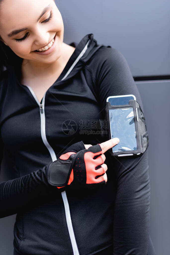 快乐女运动员用手指着手边机臂章中的智能手机图片