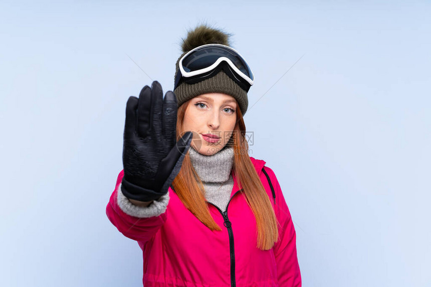穿着滑雪眼镜的雪衣红发女人在孤立的蓝墙上图片