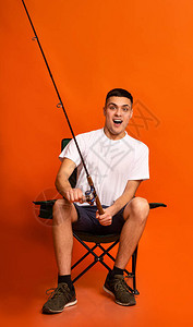 坐在椅子和钓鱼上兴奋的年轻人橙图片