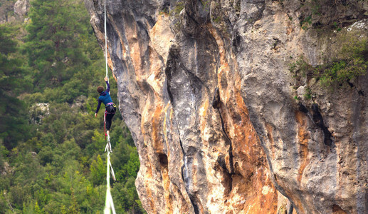 一个女人正沿着一条拉长的吊索行走山中的高线女人抓住了平衡走钢丝者在大背景图片