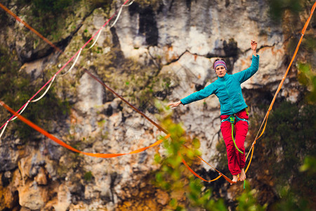一个女人正沿着一条拉长的吊索行走山中的高线女人抓住了平衡走钢丝者在大自然中的表现雷云背景上的Highliner背景图片