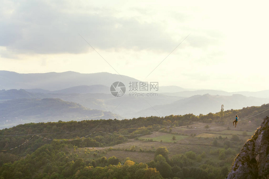 高线山脉的背景一个人坐在拉长的吊索上走钢丝的表演Highliner在深渊上保持平衡运动员摔倒图片