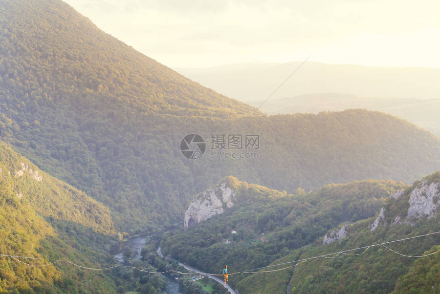 高线山脉的背景一个人坐在拉长的吊索上走钢丝的表演Highliner在深渊上保持平衡运动员摔倒图片