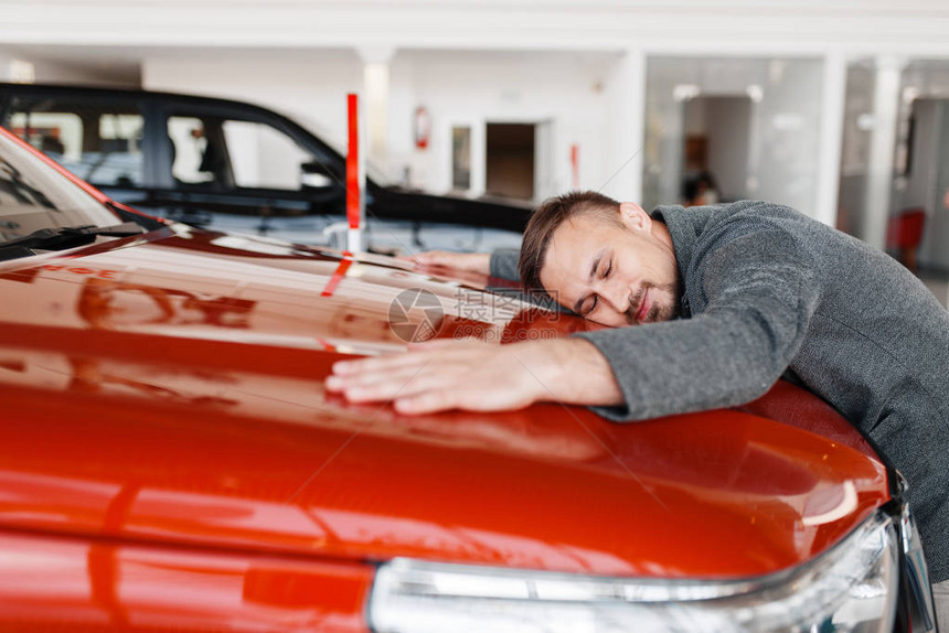男人躺在陈列室的新车引擎盖上男客户在经销商汽车销售汽车购图片