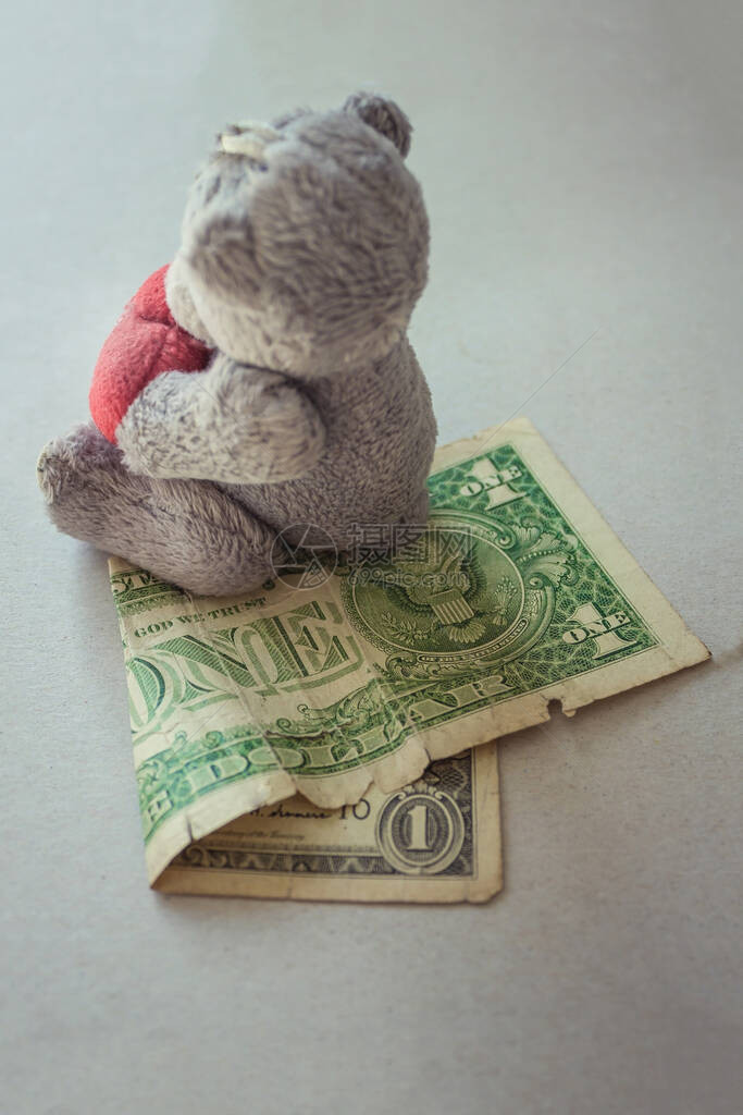 一只小玩具泰迪熊坐在一美元上图片