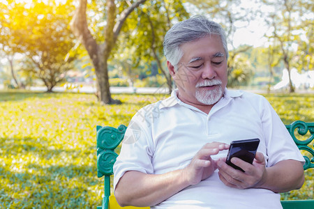 亚洲祖父在公园使用手机互联网在线给家人发短信老人通过转账申请网上银行老人在使用应程序时变背景图片