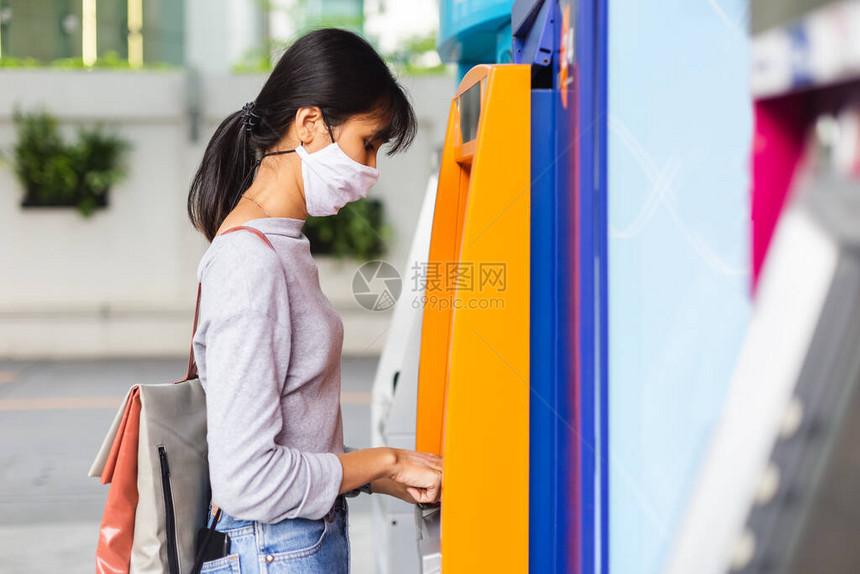 身戴防感染医疗面具的Asian妇女利用自动取款机在市图片