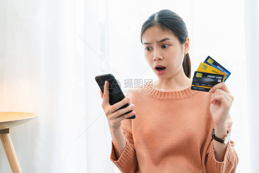 拥有信用卡和智能手机的亚洲女因为花费很多费用而感到惊骇图片