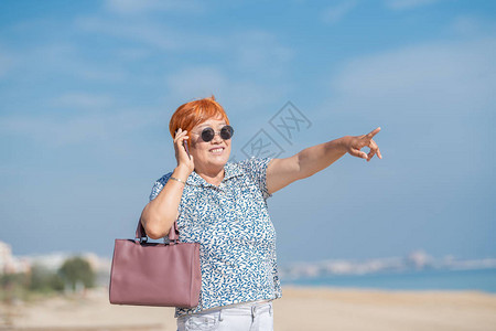 微笑的洋女人在电话上说话时指向海滩图片