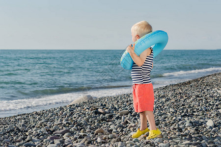 金发小男孩拿着儿童充气环站在海边图片