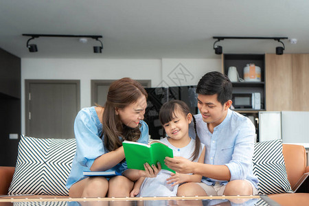 亚洲家庭与父亲母亲和女儿一起阅读关于沙发的童话尾巴故事书图片