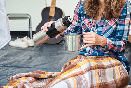 野营帐篷里从保温瓶里倒茶的女人图片