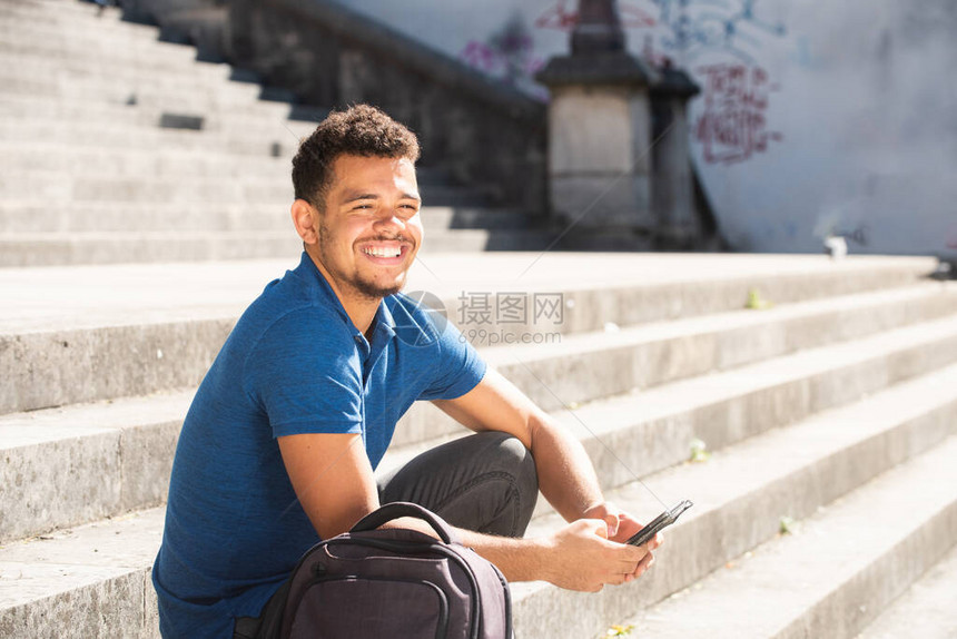 坐在外边站着手持机的台阶上的非洲年轻男子的近图片