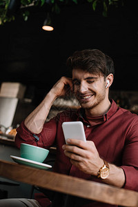 男人在无线耳机中微笑用智能手机坐在桌图片
