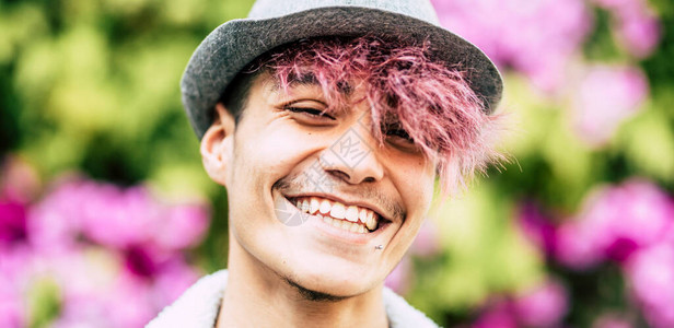 快乐英俊时尚的另类青年少肖像在彩色花卉公园背景的镜头前微笑图片