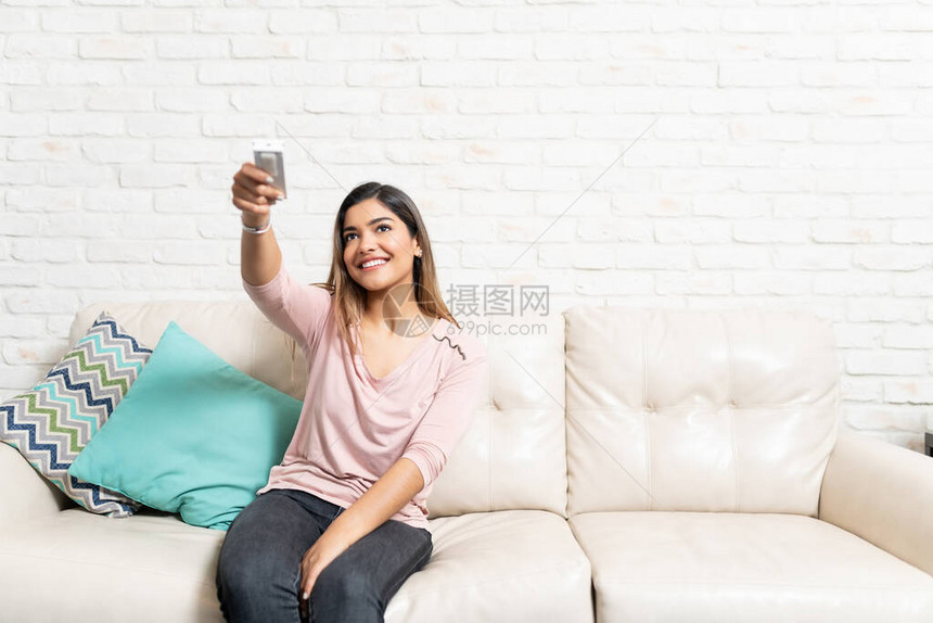坐在沙发上靠着砖墙微笑着用空调遥控图片