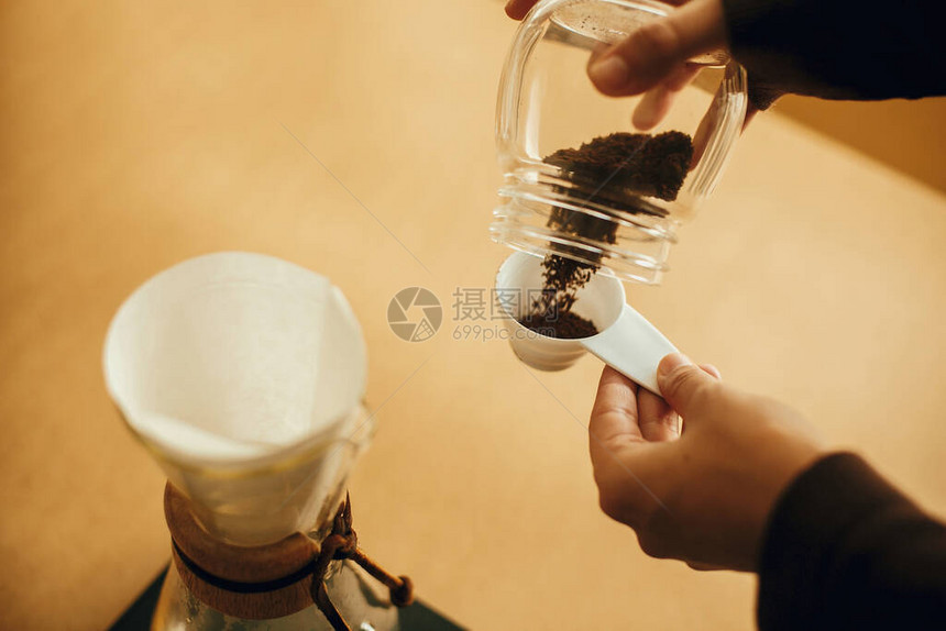 手将磨碎的咖啡倒入过滤器中准备替代咖啡冲泡v60玻璃水壶背景上拿着勺子和磨咖啡的图片