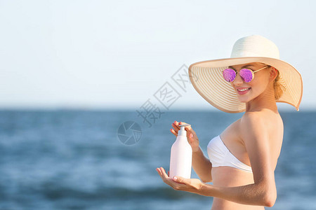 美丽的年轻女子在海滩上涂防晒霜图片