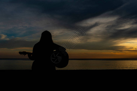 夕阳下坐在海边弹吉他的女人的剪影图片