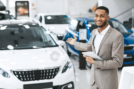 汽车销售微笑的非洲推销员在汽车经销商陈列室展示新汽车图片