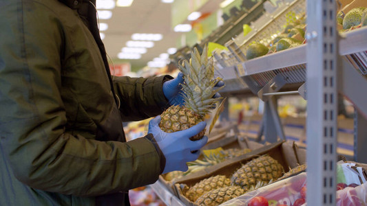 一名戴保护面罩和手套的男人在超市选择菠萝图片