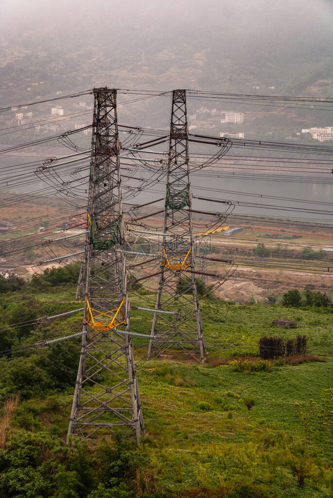 绿色山顶上河方的2个高压塔和电缆的特写地平线上的图片