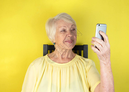 白发苍的老妇人拿着智能手机看着黄色背景图片