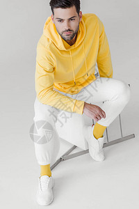 穿着黄连帽衫的英俊青年男子坐在白椅上图片