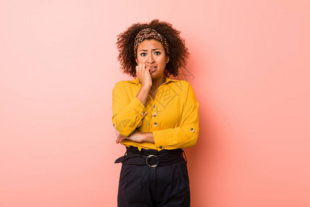 年轻非洲裔美国妇女面对粉红色背景的咬指甲紧张和焦虑不安图片