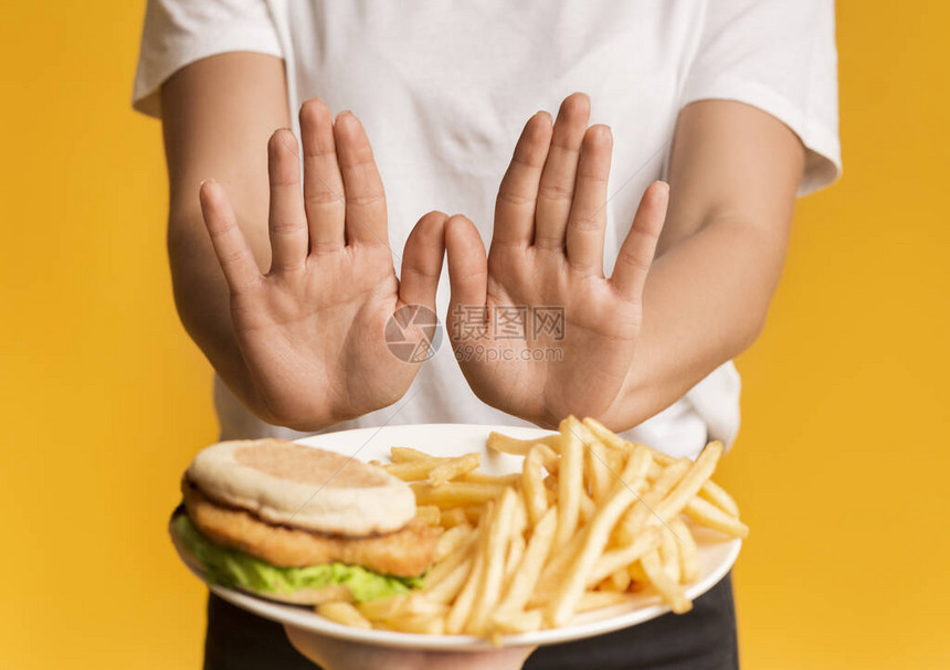 无法辨认的拒绝女用垃圾食品将牌盘装成粉末以开放棕榈展示停止手势黄色背图片