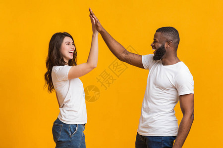 欢乐的跨种族情侣互相击掌拍手打招呼或以黄色背景欢庆胜利图片