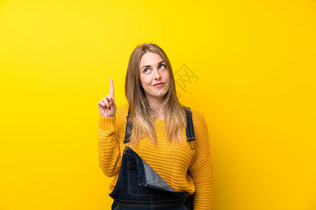 身穿孤立的黄色墙壁穿着长裤的女人用食指对图片