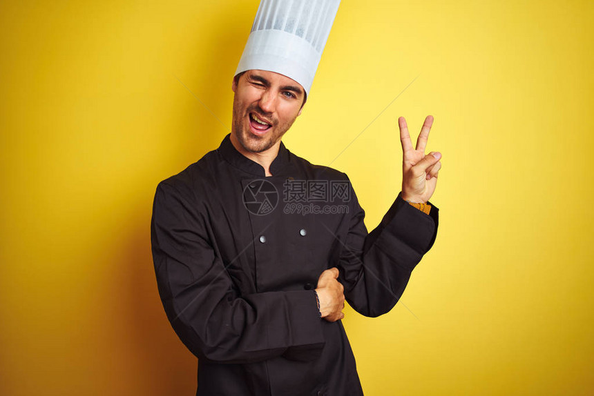 身穿制服和帽子的年轻厨师在孤立的黄色背景上站立笑着面朝镜头眨眼看图片