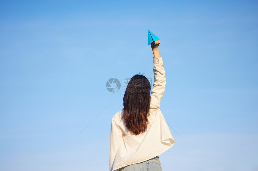 蓝天手举纸飞机的女性背影图片