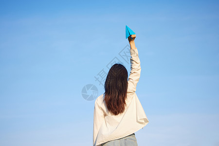 蓝天手举纸飞机的女性背影高清图片