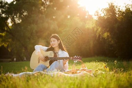 阳光下的青年美女坐在草地上弹吉他高清图片