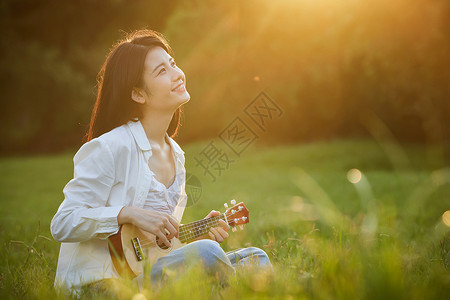 阳光下的美女坐在草地上弹吉他高清图片