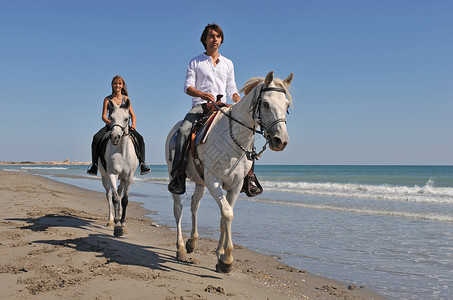 父女俩在沙滩上骑着白马背景图片
