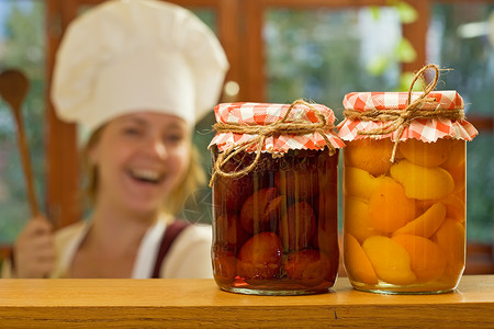 带自制水果罐头的快乐女厨师专注于罐子图片