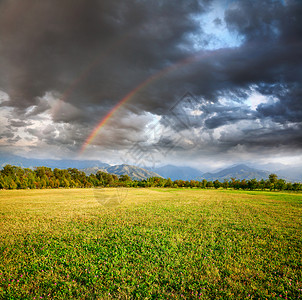 草地树木和山丘下的彩虹在乌云深图片