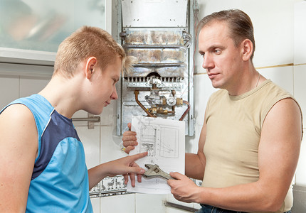 父亲和女婿一起看关于修理煤气热水器的指令图片