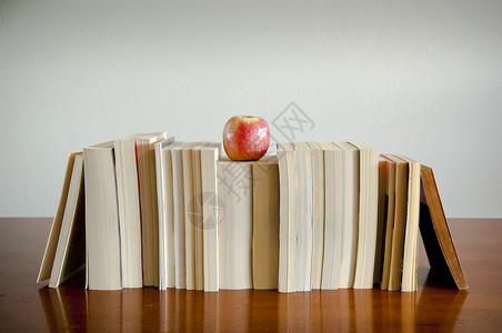 一排书上面顶有苹果的书坐在木板背景图片