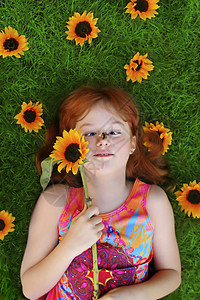 小姑娘躺在绿草上四周环绕着向日葵图片
