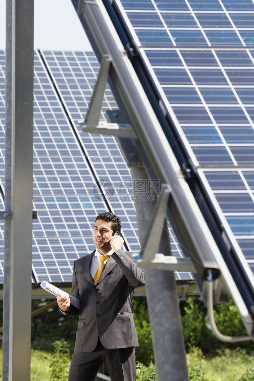 成人中意大利男工程师在太阳能发电站持有蓝图并在移动电话上交谈的肖像图片