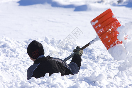 小男孩在雪地里嬉戏用铲子挖图片