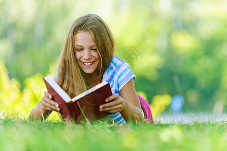 穿着蓝色上衣的美丽笑脸少女躺在草地上阅读书背景图片